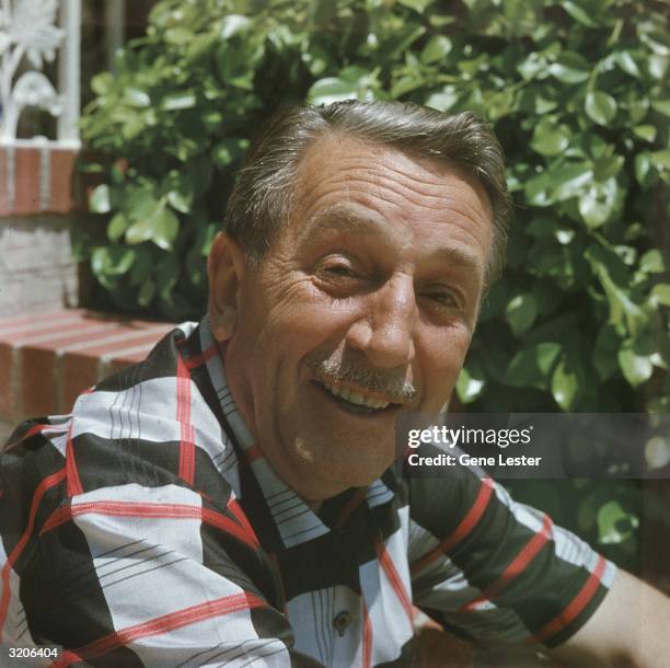 Headshot portrait of American animator and film studio founder Walt Disney smiling outdoors.