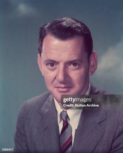 Studio headshot portrait of British-born actor and theater director Tony Randall. Randall wears a gray suit and a striped tie.