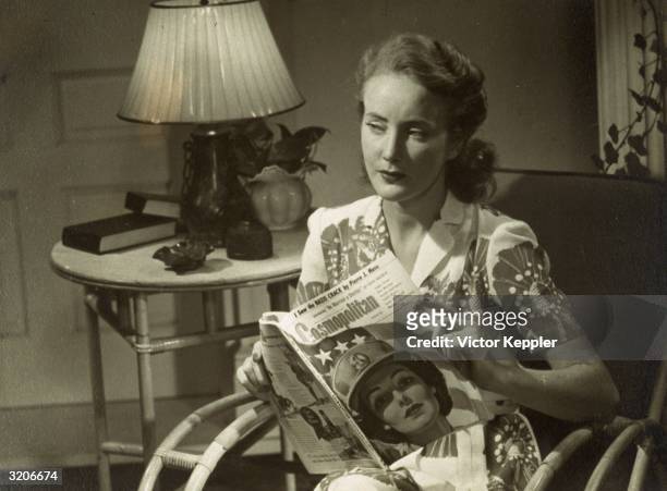 Advertisement shows a woman sitting in her living room reading an issue of Cosmopolitan magazine with an illustration of an American servicewoman on...