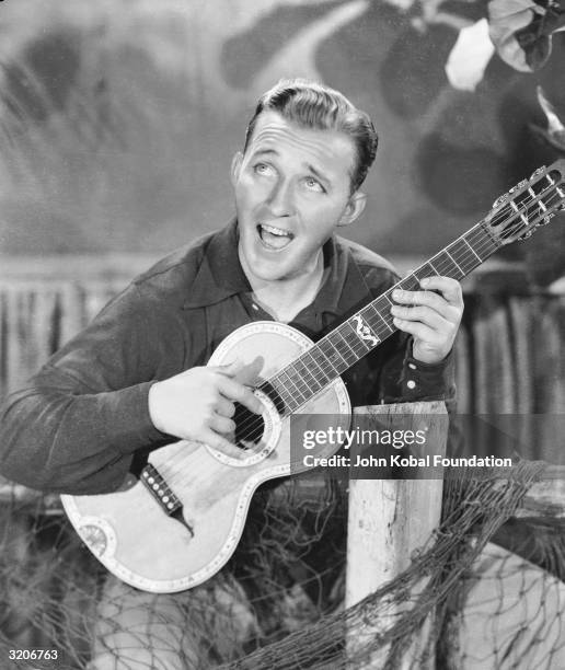 Actor and singer Bing Crosby strums a happy tune on his guitar.