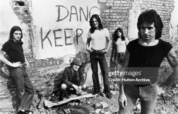 Promotional portrait of Australian hard-rock group AC/DC standing in front of a graffiti-covered brick wall, drummer Phillip Rudd, guitarist Angus...