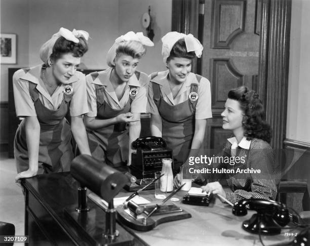 American pop vocal group the Andrews Sisters lean over a desk as they talk with American actor Harriet Hilliard in a still from director Edward F....