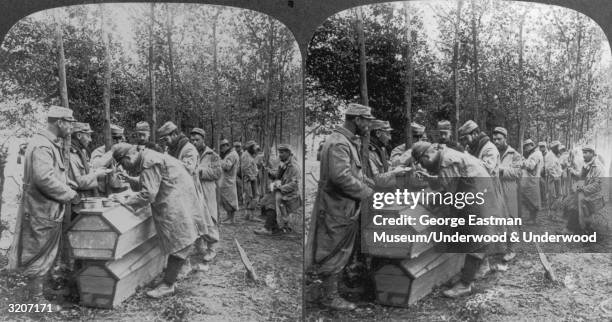 Full-length stereoscope images of French soldiers using coffins as a table during a meal in the Argonnex forest, France, World War I.