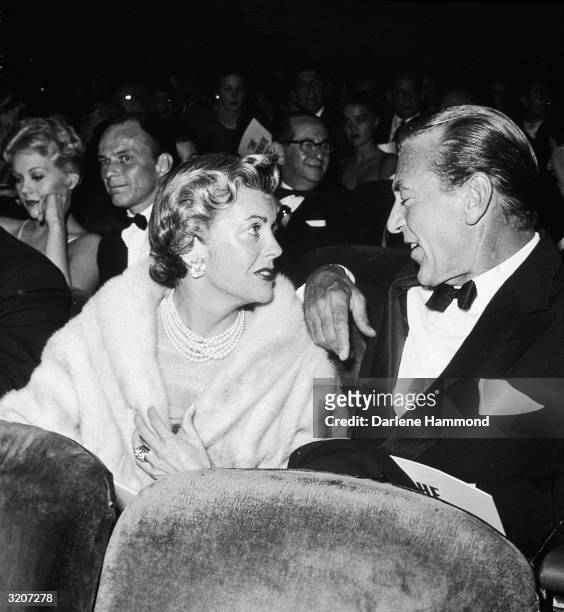 American actor Gary Cooper sitting in a theatre and talking to his wife, Rocky (also known as Veronica Cooper, or actor Sandra Shaw, , at the...