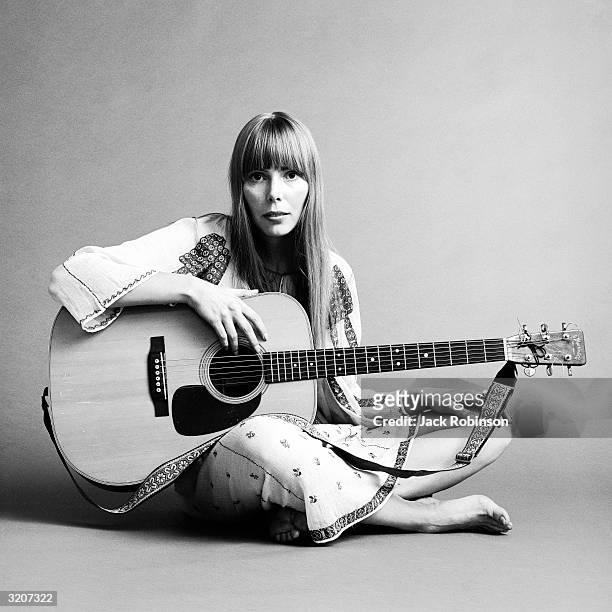 Portrait of American musician Joni Mitchell seated on the floor with her acoustic guitar in her lap. This image was from a shoot for the fashion...