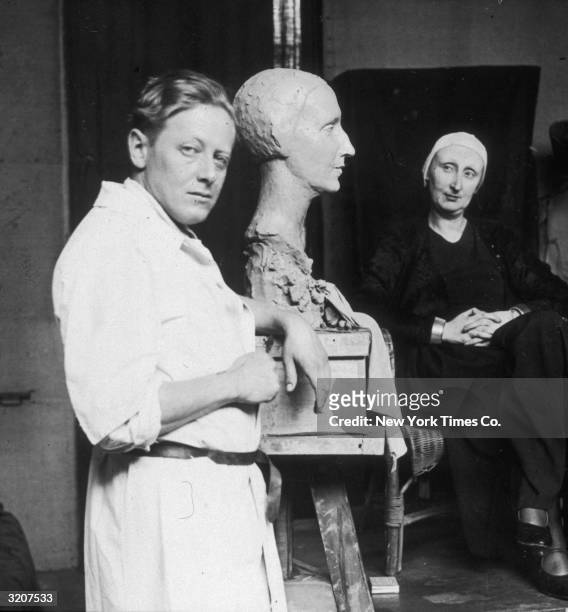 Portrait of American sculptor G Fite Waters leaning next to the bust of writer Edith Sitwell upon which he is working, while Sitwell sits in the...