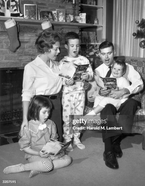 Full-length image of a family singing Christmas carols in their living room, 1960s. The father holds a young child in his lap, as the mother kneels...