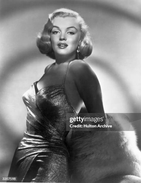 Studio glamour portrait of American actor Marilyn Monroe , wearing a lame evening dress and fur wrap, early 1950s.
