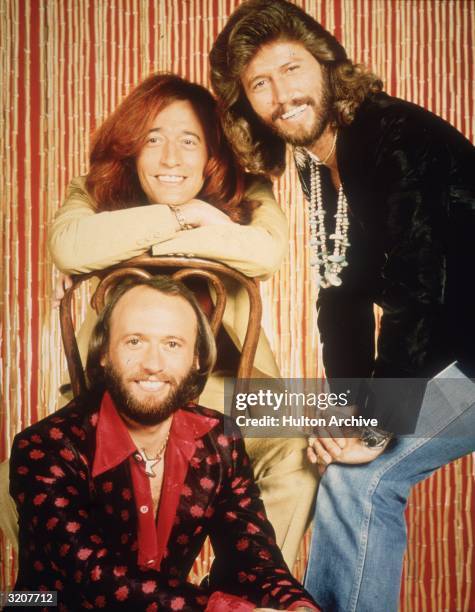 Portrait of the brothers Barry, Robin and Maurice Gibb, who comprise the pop group The Bee Gees, in front of a bamboo curtain.