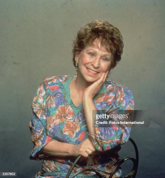 Studio portrait of American actor Alice Ghostley, wearing a printed blouse, sitting in a chair with her hand to her face.