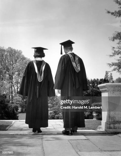 Full-length image of two graduates standing in their mortars and robes outdoors on a staircase.