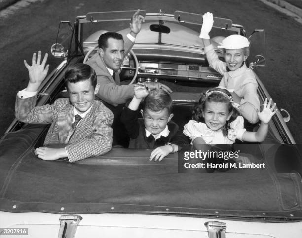 Family waves while looking back in their convertible.