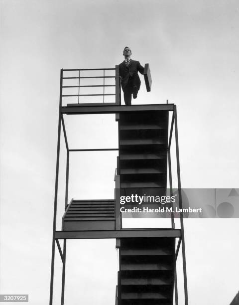 Businessman wearing a suit and carrying a briefcase walks off the top of a staircase that leads to nowhere.