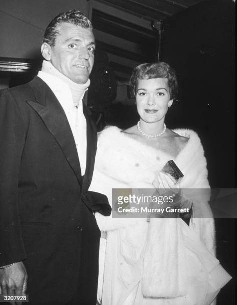 American actor Jane Wyman and Greg Bautzer, wearing a neck brace, stand together and smile while at the Damon Runyon Cancer Fund benefit party held...