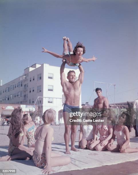 Body builder DeForrest Most lifting Alice Ferges over his head before a group of spectators, Muscle Beach, Santa Monica, California.