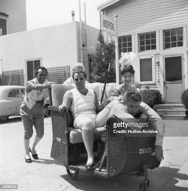 American actors Marlon Brandon, James Dean and an unidentified woman are pushed in a wheeled wicker chair by two men on the set of director Henry...