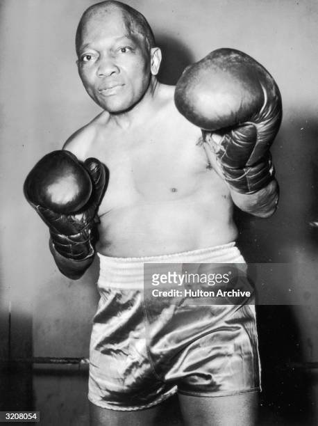 Portrait of heavyweight boxer Jack Johnson in uniform, holding up gloved fists, Brooklyn, New York.
