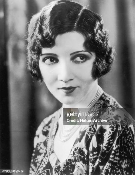 Headshot portrait of American actor Claudette Colbert with a bob haircut, wearing a patterned dress.