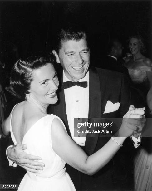 American actor and politician Ronald Reagan smiling and dancing with his wife Nancy at a charity party. Reagan is dressed in a tuxedo. His wife is...