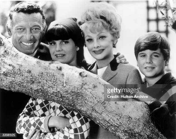 Outdoor portrait of American comedic actor Lucille Ball posing behind a tree branch with her second husband Gary Morton , and her children Lucie...