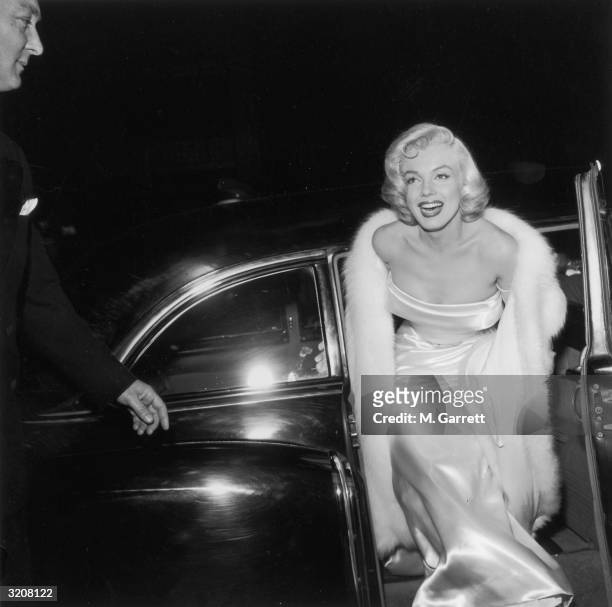 American actor Marilyn Monroe emerges from a car, wearing a strapless white gown and white fur coat at the premiere of director Walter Lang's film...