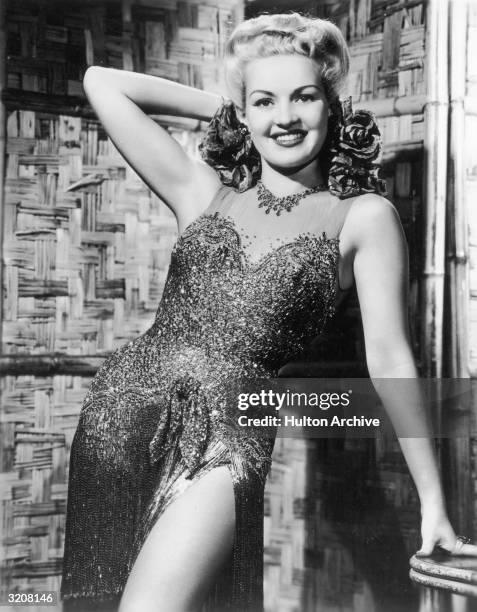 Promotional portrait of American actor Betty Grable posing in a slit sequined dress.