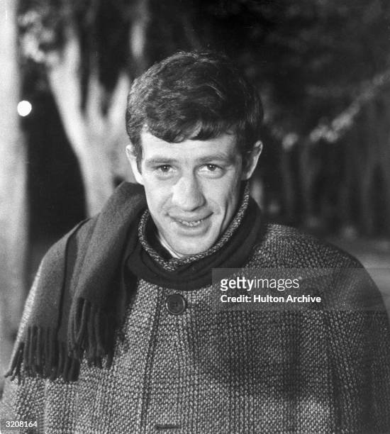 French actor Jean-Paul Belmondo wearing a winter coat and scarf outdoors.