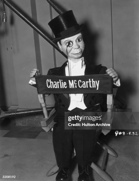 Portrait of Charlie McCarthy, dummy of American ventriloquist Edgar Bergen, sitting backwards in a personalized director's chair on the set of...