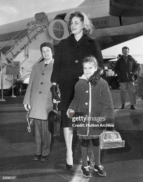 Full-length image of American actor Lauren Bacall posing with her children, Stephen and Leslie Bogart, on the airstrip at New York International...