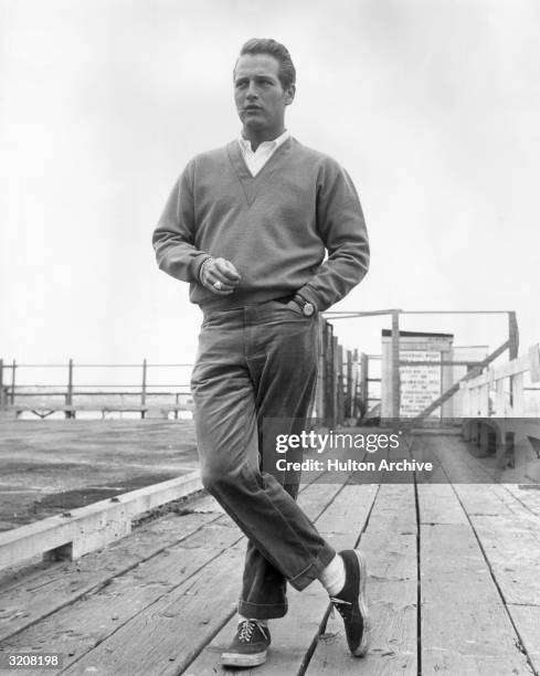 Full-length portrait of American actor Paul Newman, wearing a button-down shirt, a V-neck sweater, corduroy pants, and sneakers, holding a toothpick...