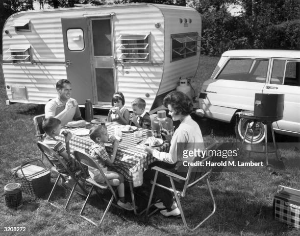 Family has a picnic outdoors next to their trailer.