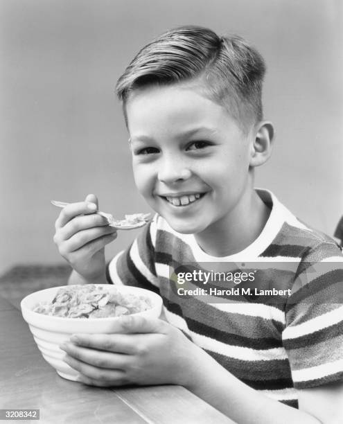 Studio portrait of a young boy smiling while eating a bowl of cereal.