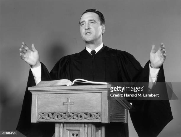 Studio portrait of a clergyman in a robe gesticulating while delivering a sermon at the pulpit.