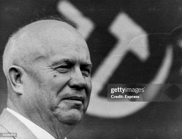 Headshot of former Soviet Premier Nikita Khrushchev with the hammer and sickle symbol behind him.