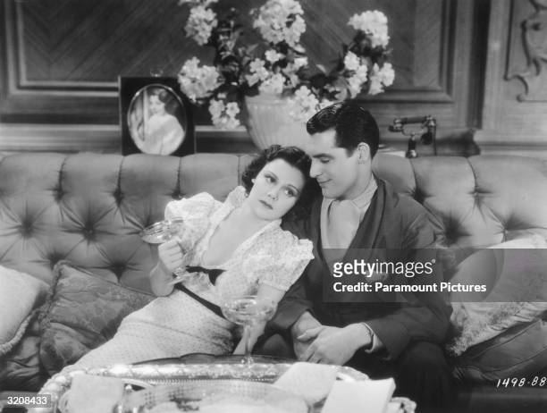 American actor Helen Mack and British-born actor Cary Grant lounge on a sofa and drink champagne in a still from the film, 'Kiss and Make Up,'...