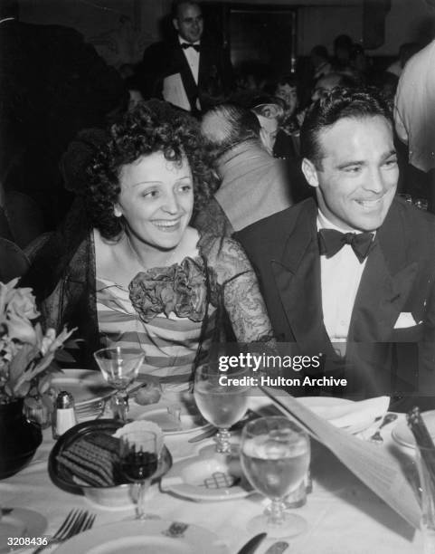 French singer Edith Piaf and French boxer Marcel Cerdan smile while sitting at a dining table at the Versailles nightclub, New York City.