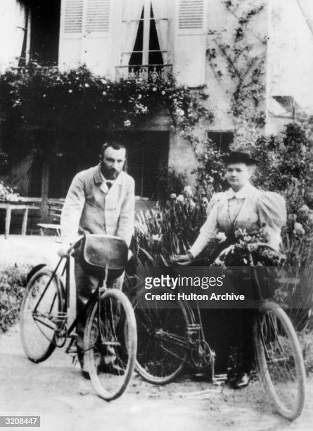 Married chemists Pierre Curie and Marie Curie standing outdoors with bicycles on their honeymoon.