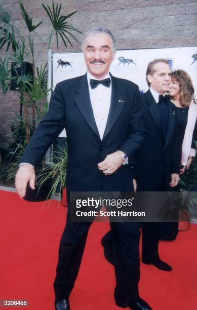 Full-length image of American actor Burt Reynolds adjusting a button on his blazer and smiling while arriving on the red carpet at the eighth annual...