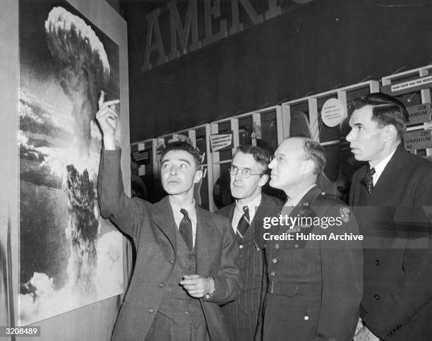 American physicist Dr. Robert Oppenheimer , points to a picture of the atomic bomb explosion over Nagasaki, Japan, as scientist Henry D. Smyth ,...