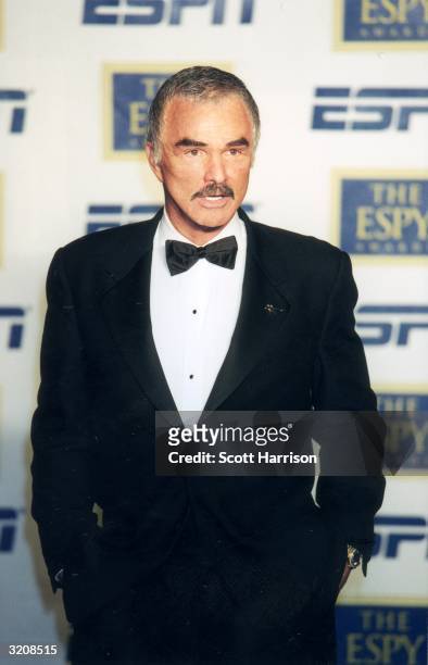 American actor Burt Reynolds standing with his hands in his pockets and talking in front of a wall of logos at the eighth annual ESPY Awards, where...