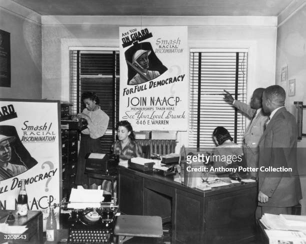 View inside an office of the National Association for the Advancement of Colored People where a man points to a sign reading, 'Are You ON GUARD;...