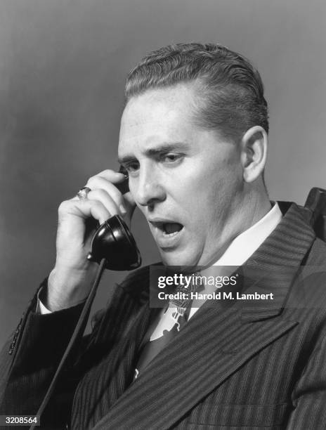 Studio headshot of a businessman speaking into a telephone receiver, 1940s.