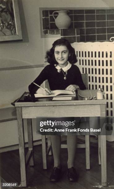 German diarist and Holocaust victim Anne Frank sits at a wooden desk, writing in a journal, 1940.