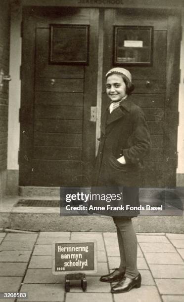 Full-length portrait of Margot Frank, the older sister of Anne Frank, standing in front of the doorway of the Jeker school with her hands in her coat...