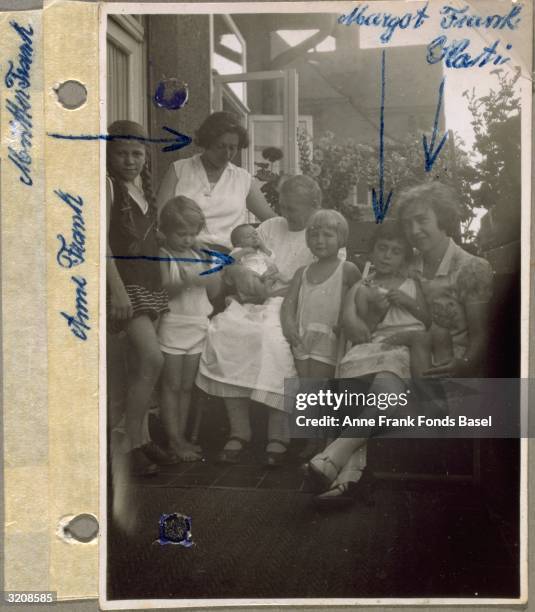 Photo from Anne Frank's photo album of Anne Frank , held by a woman , being welcomed by her sister Margot's friends on a balcony, with names written...