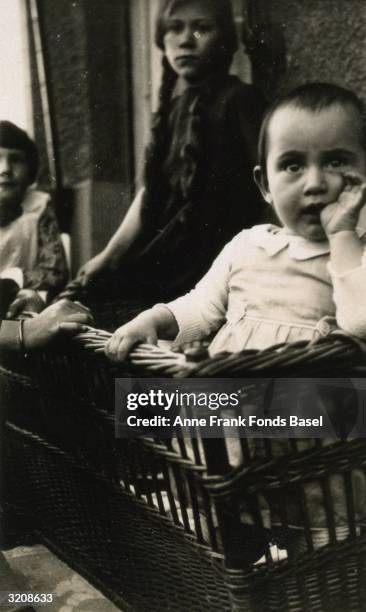 Anne Frank sucking her thumb in a wicker cradle in front of other children on a balcony, Frankfurt am Main, Germany. From Anne Frank's photo album.