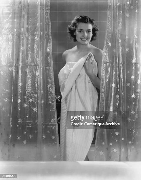 Woman smiles as she stands between two shower curtains, wrapped in a towel.