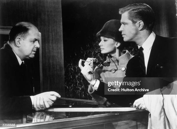 Belgian-born actor Audrey Hepburn and American actor George Peppard stand at the Tiffany's sales counter, speaking with American actor John McGiver...