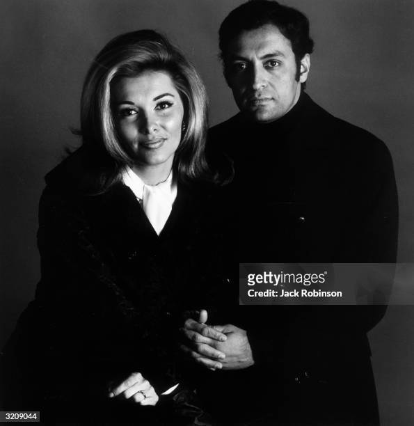 Studio portrait of Indian conductor Zubin Mehta posing beside his wife, Nancy Kovack. She wears a white ascot, and Mehta wears a dark peacoat and...