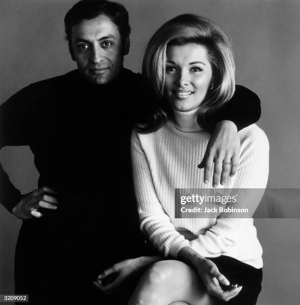 Studio portrait of Indian conductor Zubin Mehta posing with his arm around the shoulder of his wife, Nancy Kovack. She wears a white turtleneck...